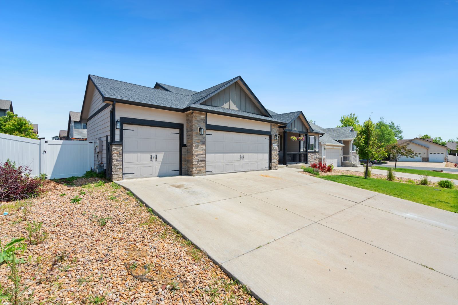 Modern craftsman ranch home with stone accents and two taupe garage doors (a double and a single) facing a clean concrete driveway, deep blue sky.