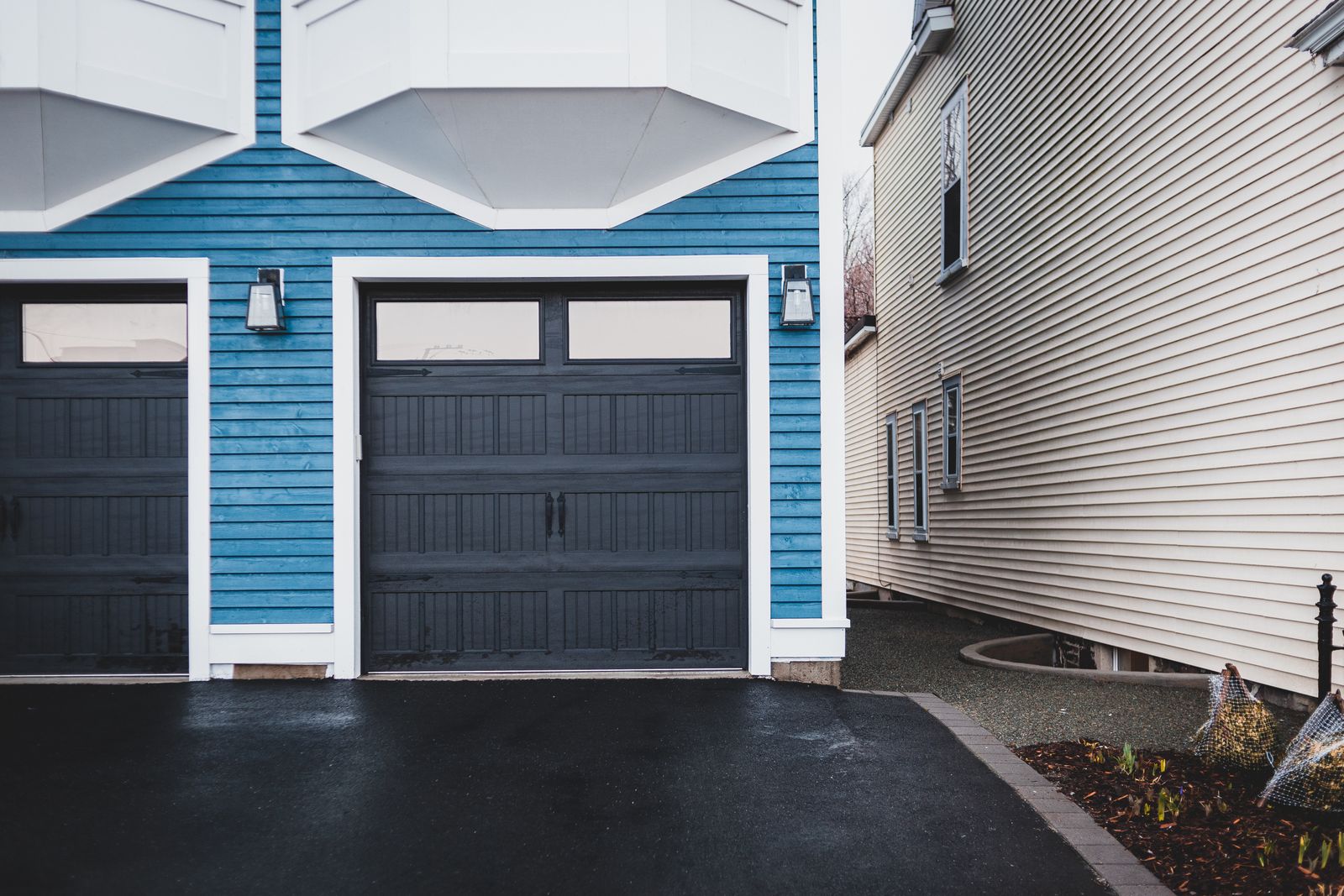 Crisp modern blue-clapboard home with black carriage-style garage doors and white trim, dark asphalt driveway. Tight, clean composition focused on the doors.