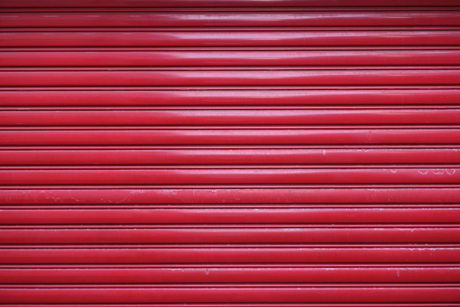 Full-frame close-up of a glossy bright-red rolling steel shutter, horizontal slats with strong highlights.