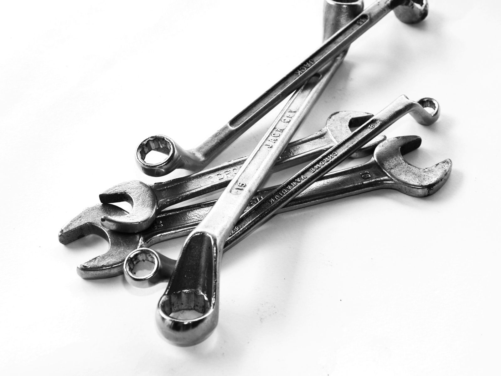 Studio close-up of a stack of chrome combination wrenches crossed over each other on a clean white background, black-and-white/desaturated.